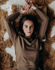Woman lying on a textured brown rug wearing a brown sweater.