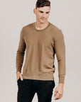 Man wearing a brown sweater and black pants against a plain background
