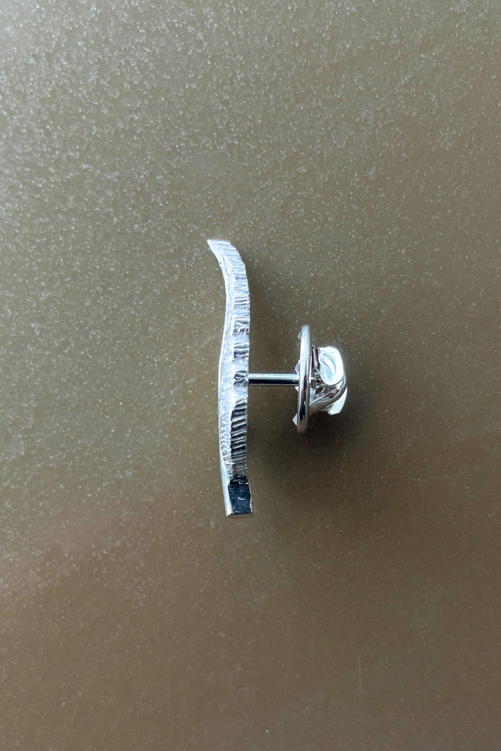 Silver earring with a curved design on a beige background
