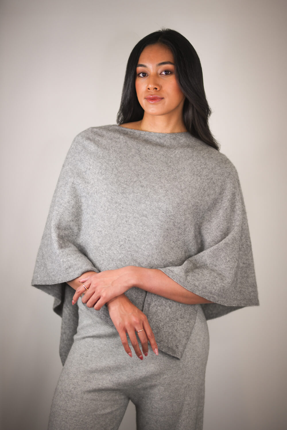 Woman wearing a gray poncho against a plain background