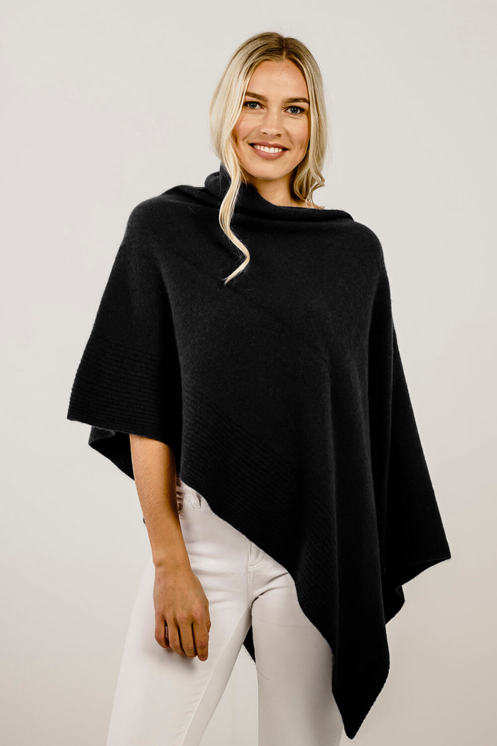 Woman wearing a black merino poncho against a plain background