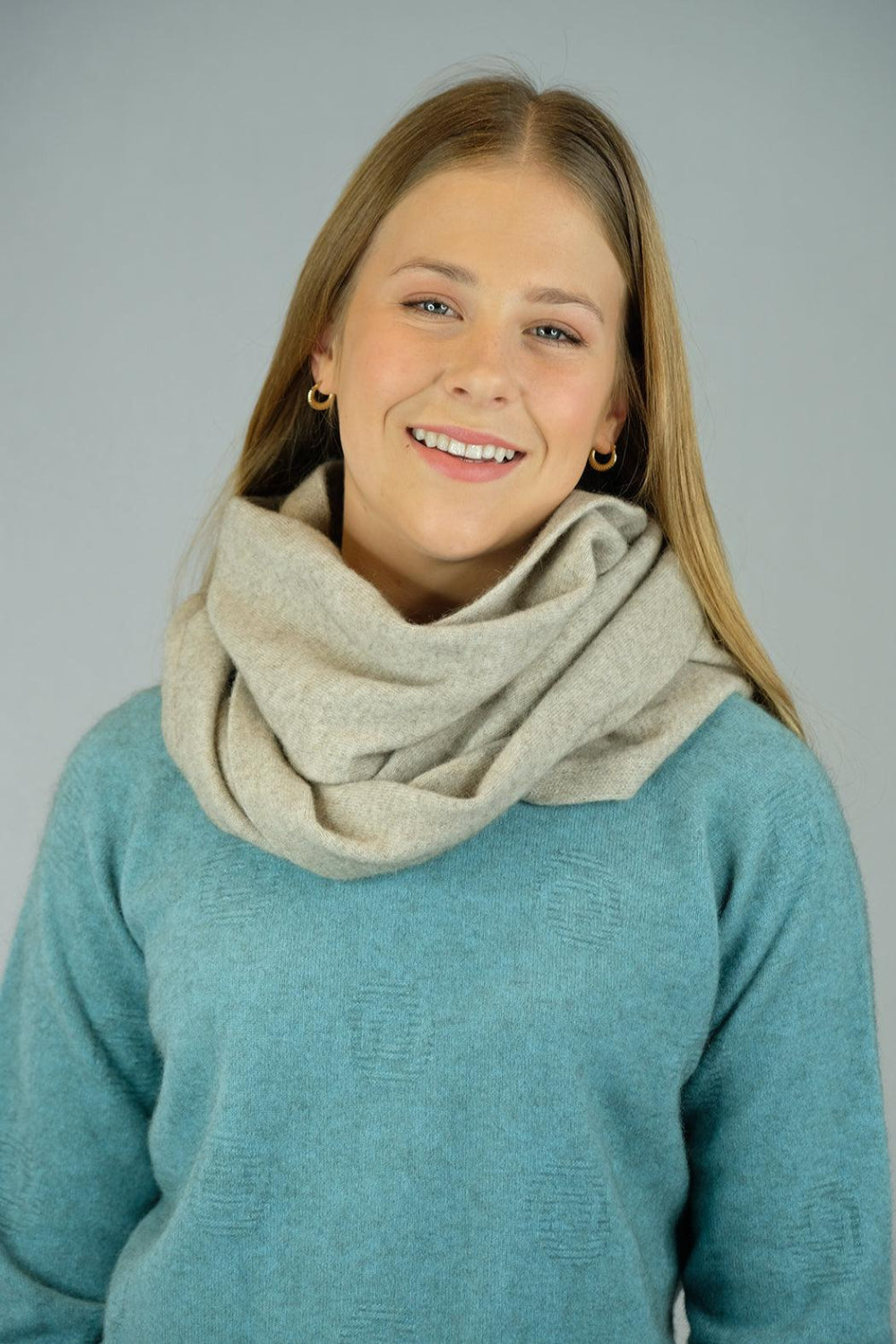A woman wearing a super-fine merino wool loop scarf in a soft blue color, smiling.