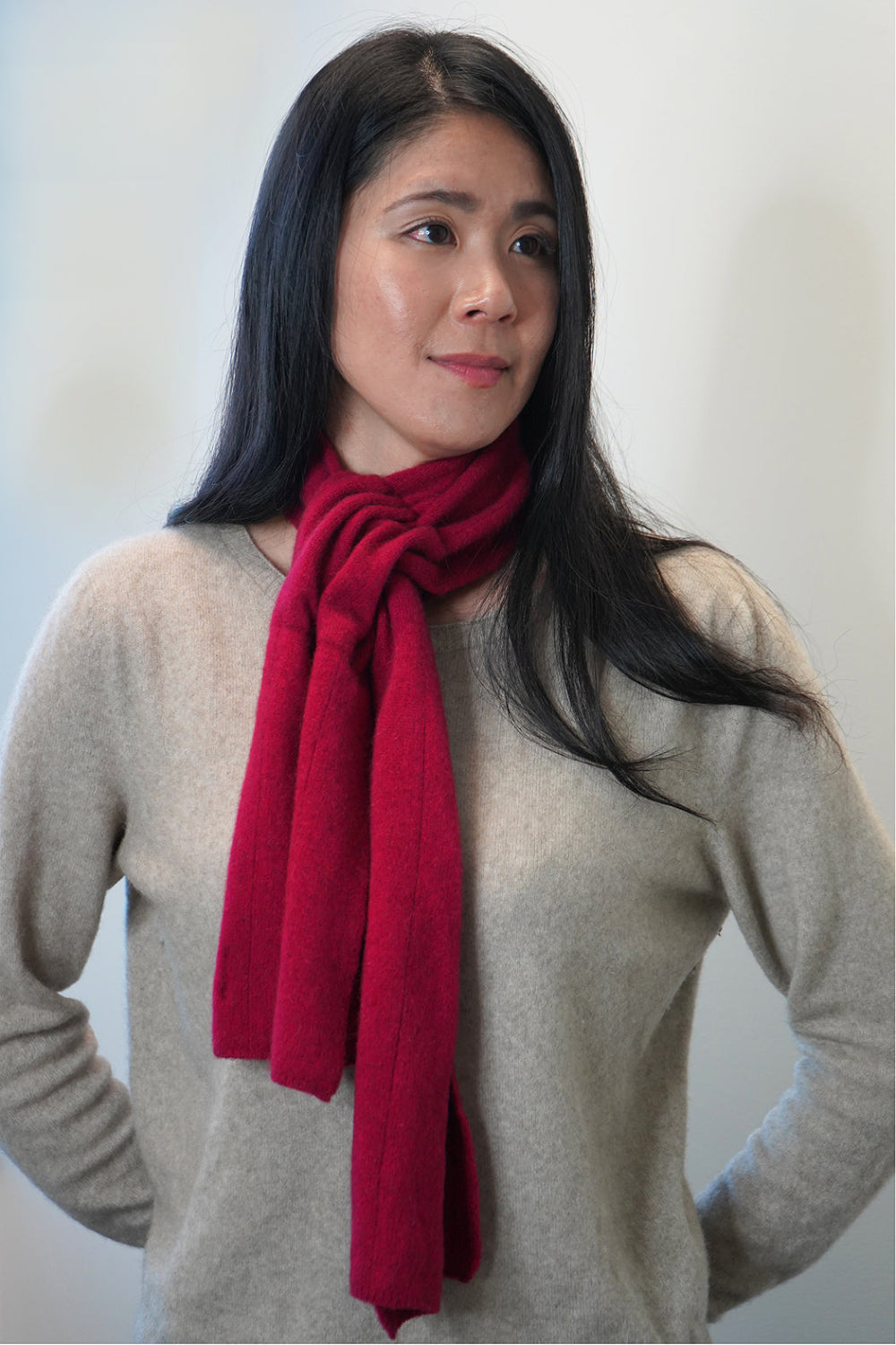 Woman wearing a red scarf and beige sweater against a plain background