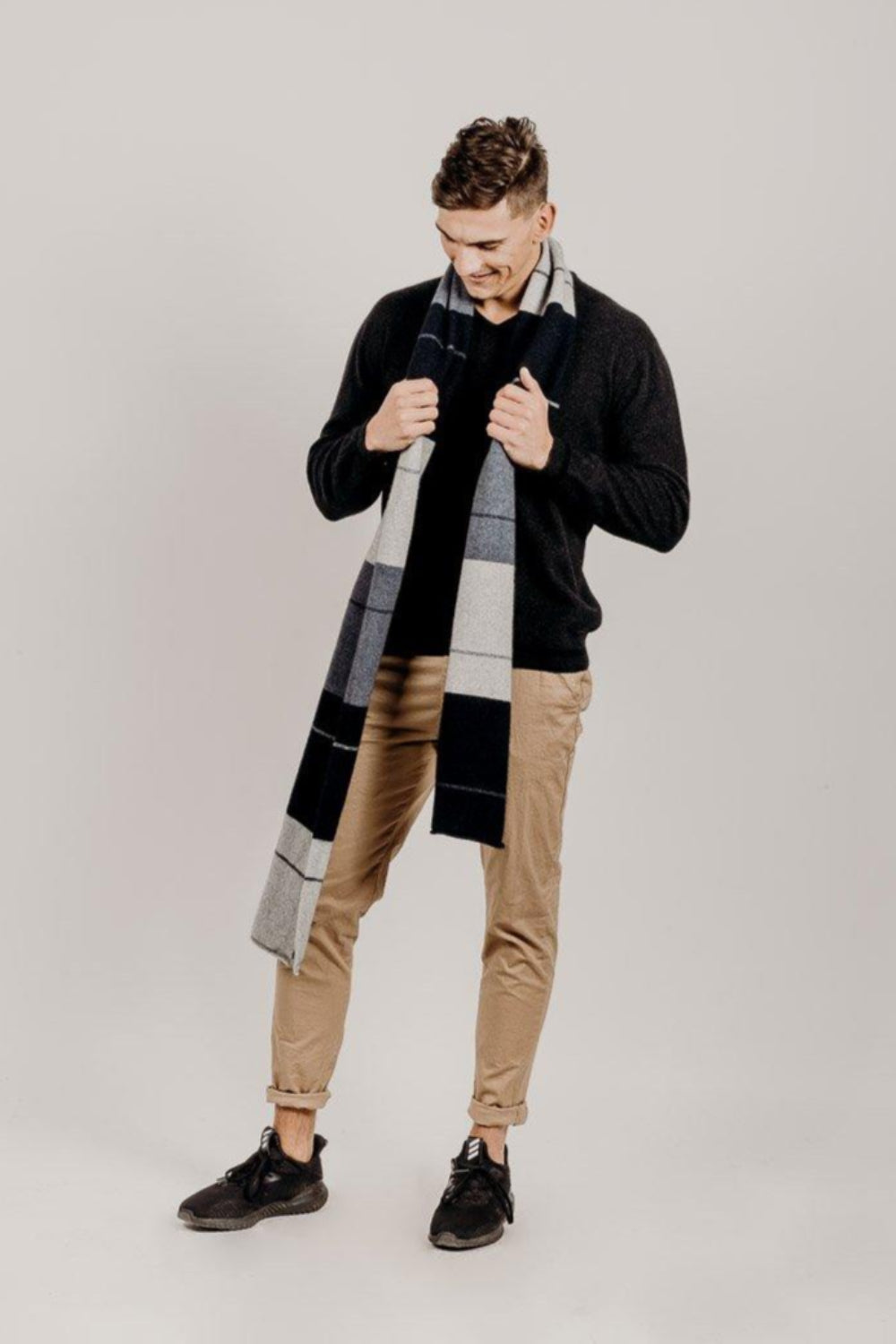 Man wearing a charcoal sweater and plaid scarf against a plain background