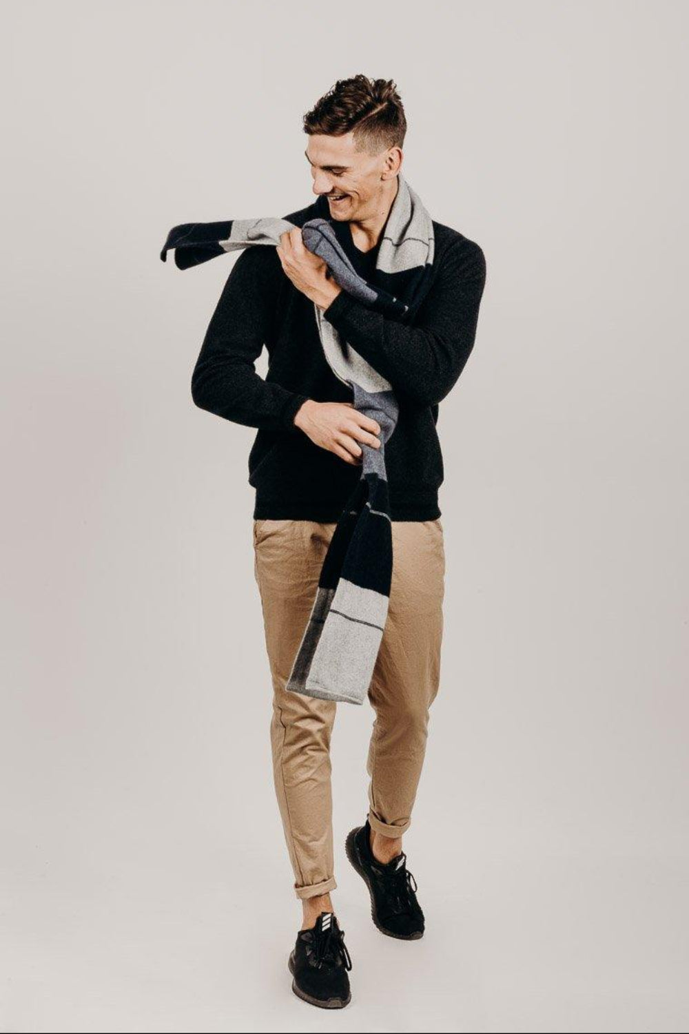 Man wearing a black sweater and plaid scarf against a plain background