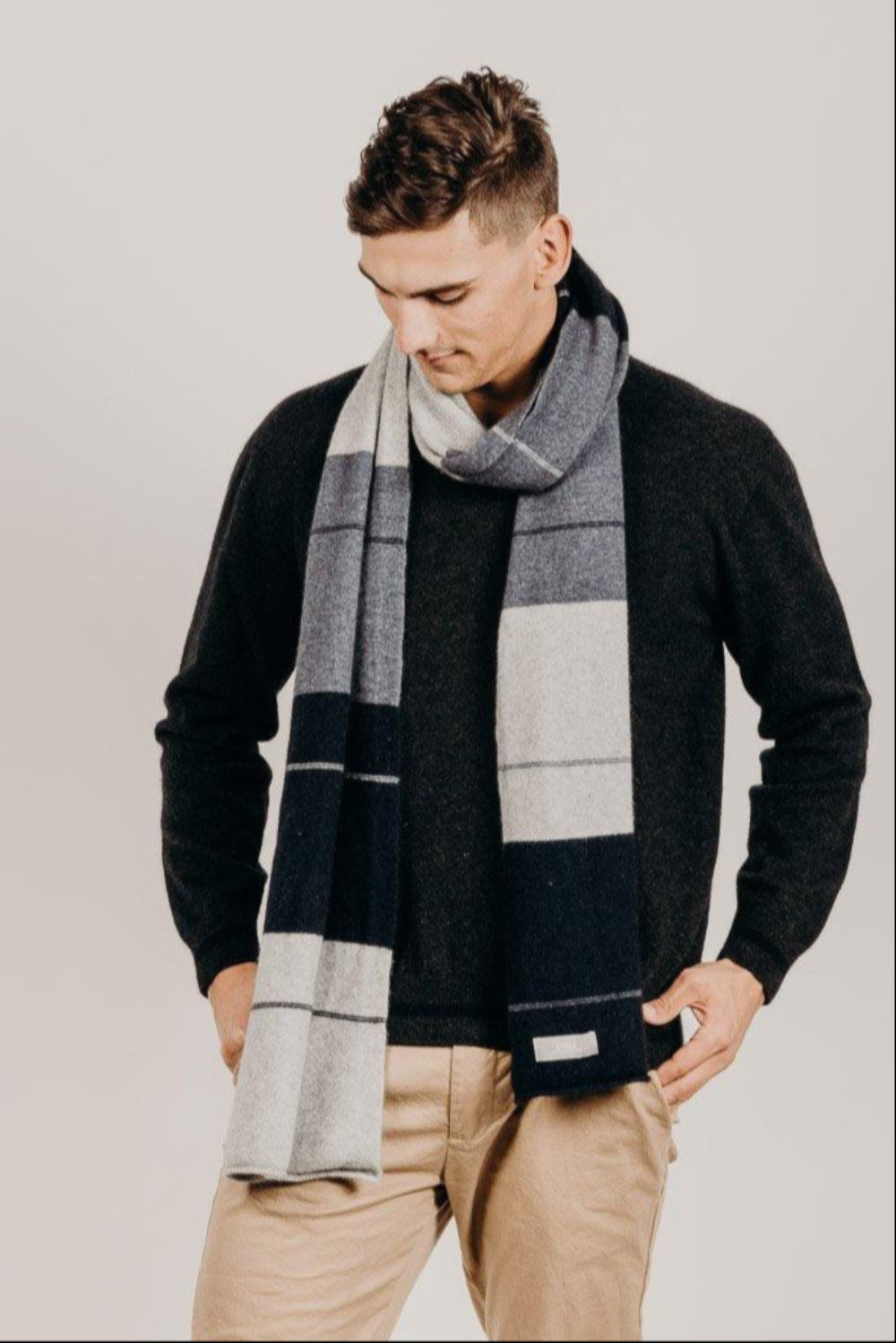 Man wearing a charcoal sweater and plaid scarf against a plain background