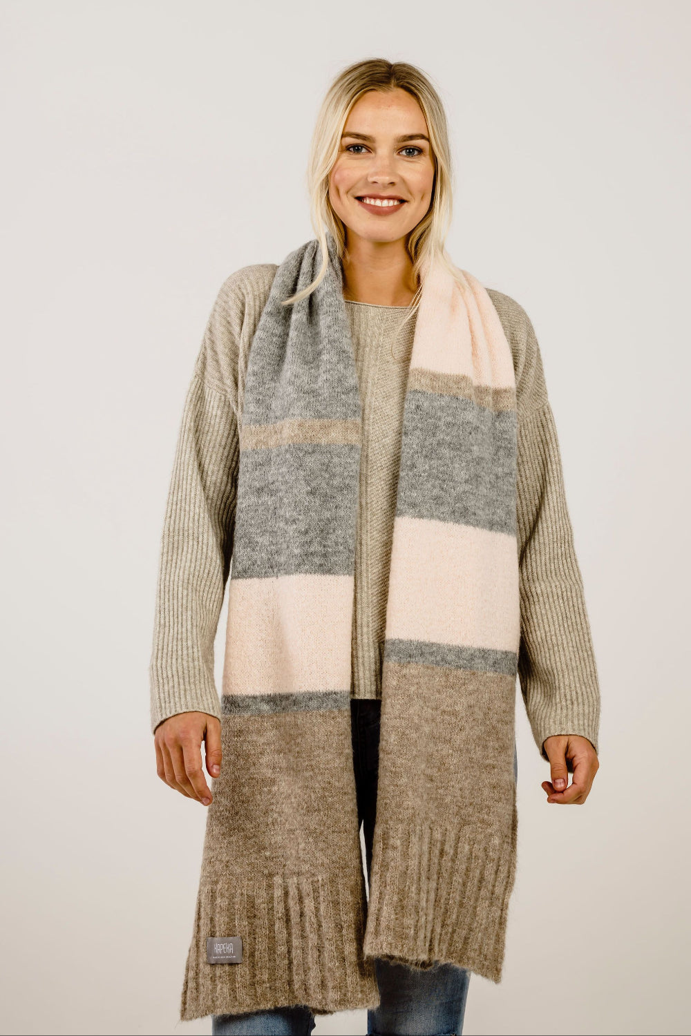 Woman wearing a beige sweater with a scarf on a plain background