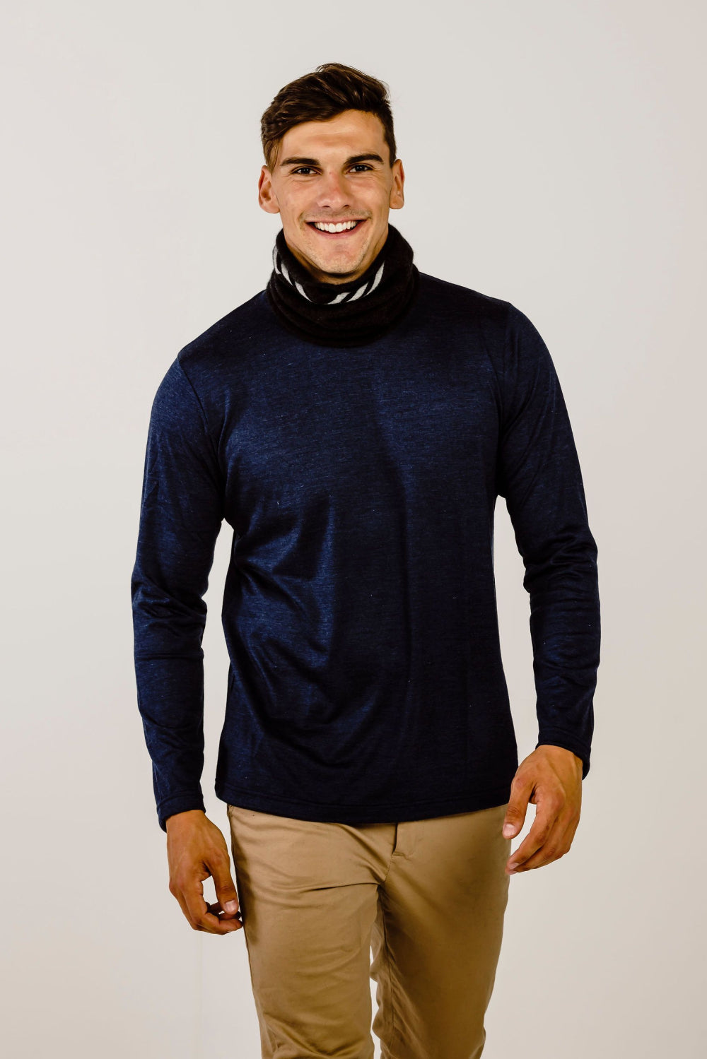 A man wearing a black Merinosilk neck warmer with grey stripes, smiling against a white background.