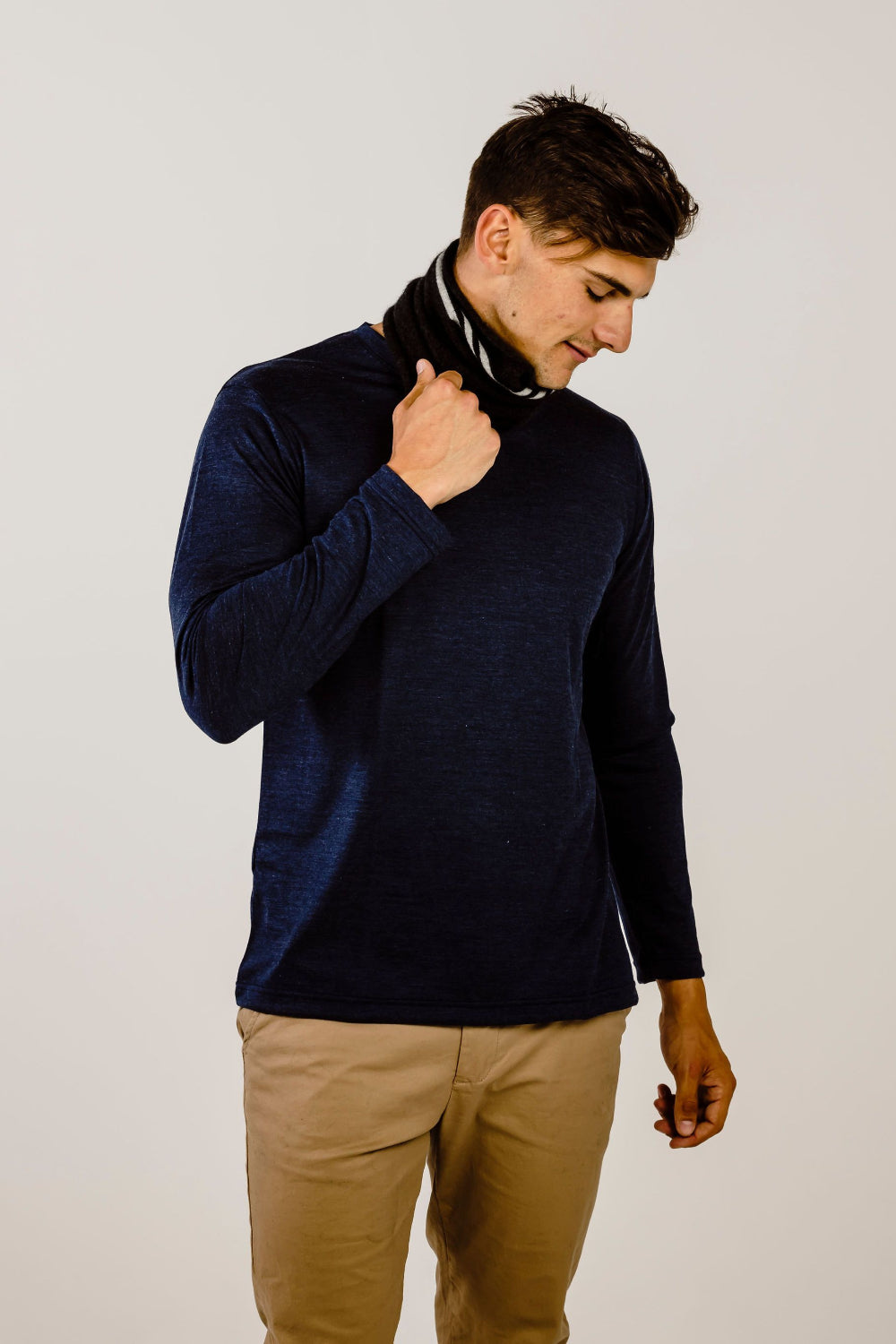 Man wearing a navy sweater and beige pants against a plain background
