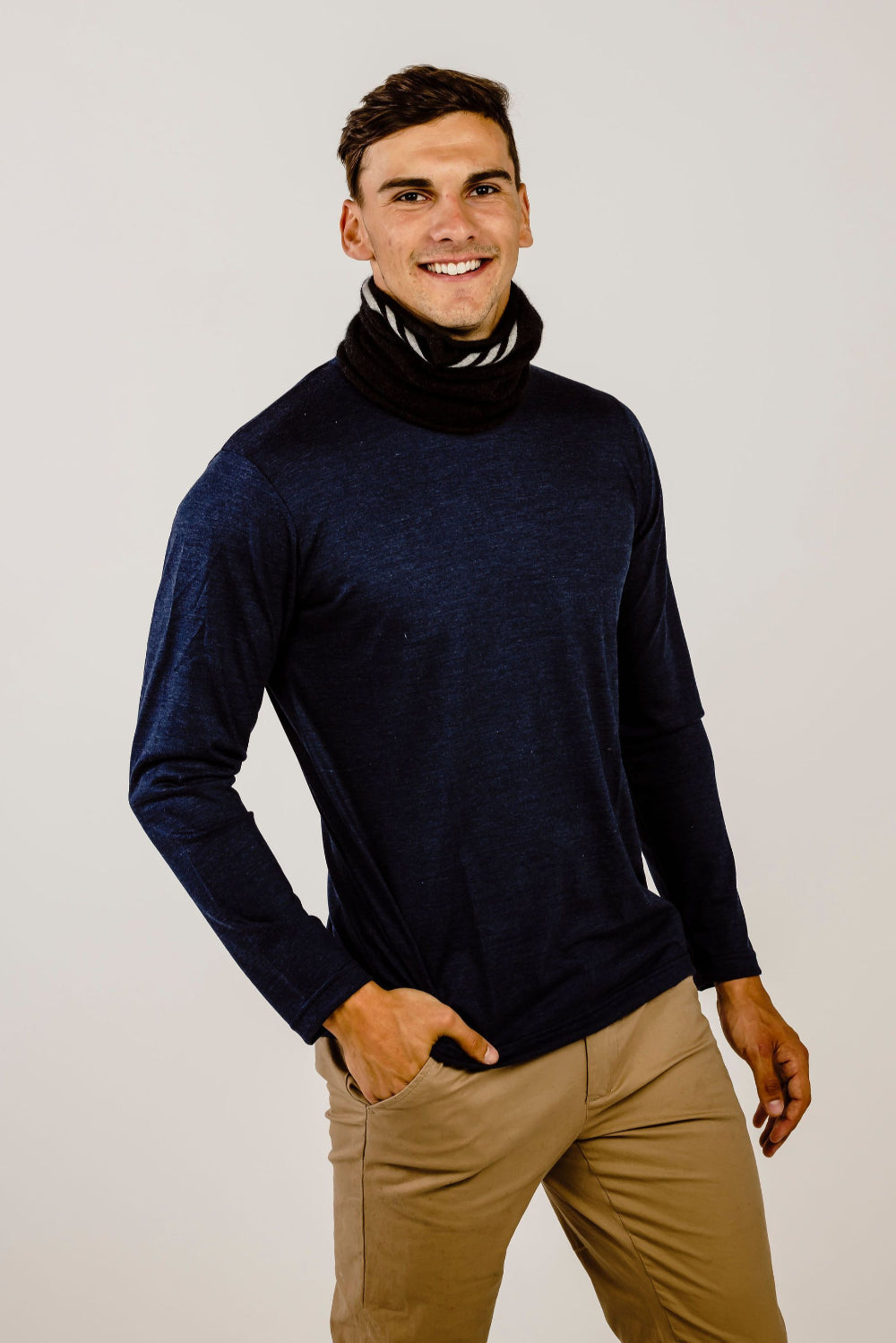 Man wearing a navy turtleneck sweater and beige pants against a plain background