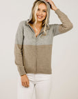 Woman wearing a two-tone zip-up hoodie with gray and beige colors on a plain background