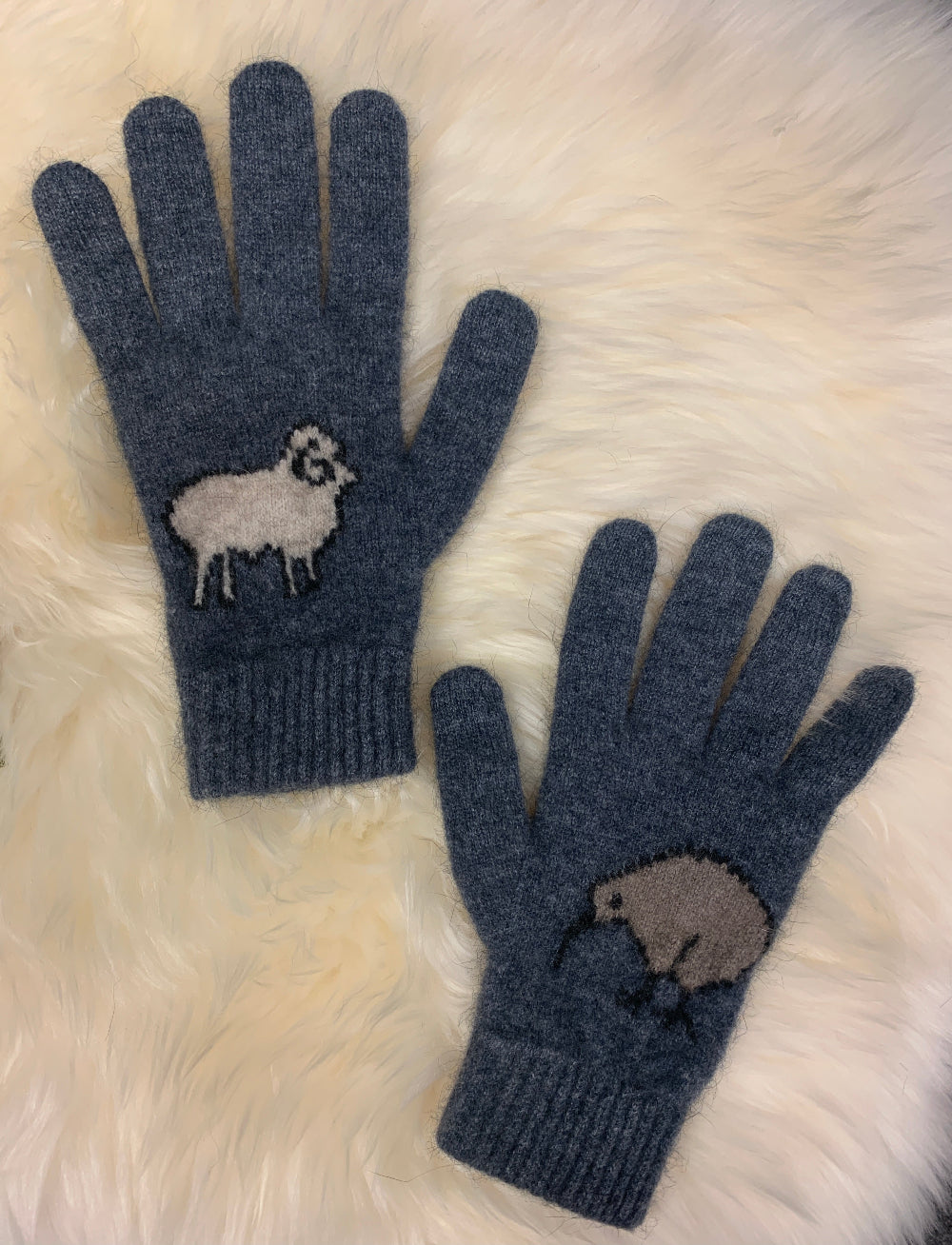 Pair of blue gloves with embroidered sheep design on a fluffy white surface